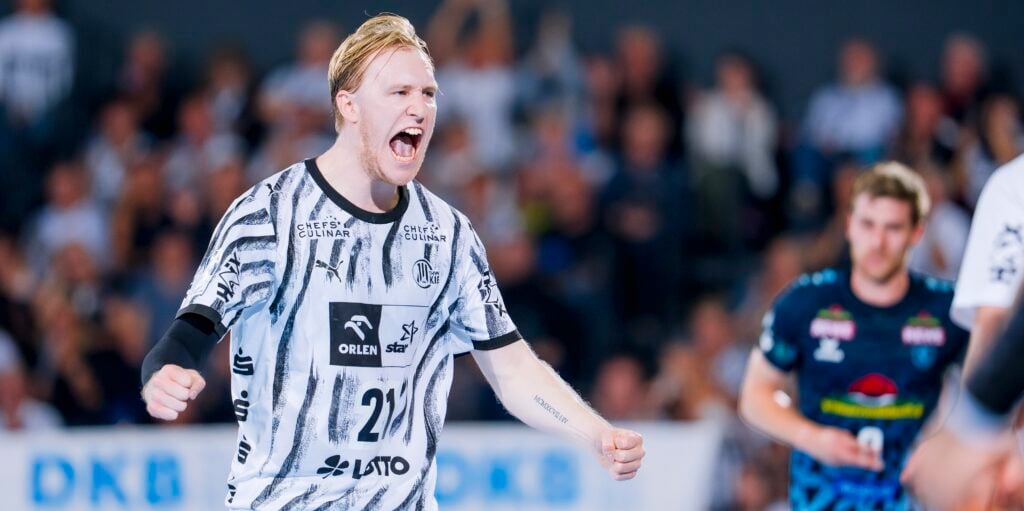 Ein Handballspieler in einem schwarz-weißen Trikot feiert mit begeistertem Gesichtsausdruck und geballten Fäusten auf dem Spielfeld.