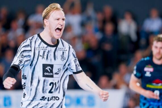 Ein Handballspieler in einem schwarz-weißen Trikot feiert mit begeistertem Gesichtsausdruck und geballten Fäusten auf dem Spielfeld.