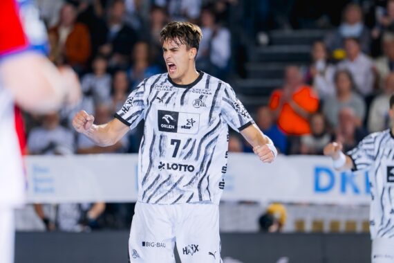 Ein Handballspieler in einem weiß gemusterten Trikot jubelt und feiert während eines Spiels auf dem Spielfeld.