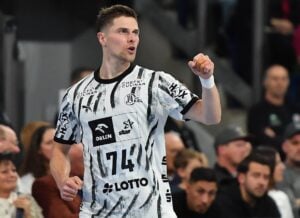 Ein Handballspieler in einem weißen Trikot mit der Nummer 74 feiert mit erhobener Faust.