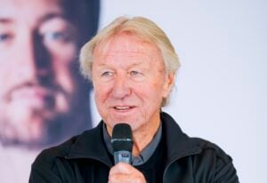 Ein älterer Mann mit blonden Haaren, der in ein Mikrofon spricht.