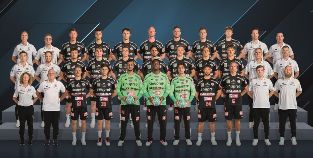 26_vor_HCE_Teambild Mannschaftsfoto der Handballspieler und Betreuer des HC Erlangen in schwarzen und limettengrünen Trikots.