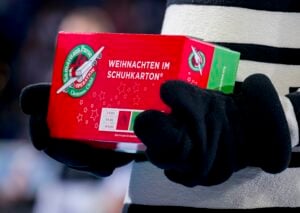 Eine Person mit schwarzen Handschuhen hält einen roten Operation Christmas Child-Schuhkarton mit der Aufschrift Weihnachten im Schuhkarton in der Hand.