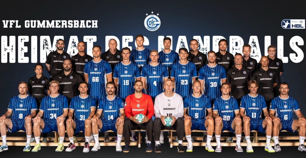 VFL_Gummersbach_Teambild_45x29 Mannschaftsfoto des Handballvereins VfL Gummersbach, auf dem Spieler und Trainer in blauen Trikots in Reihen sitzend und stehend zu sehen sind; hinter ihnen ist in großen Buchstaben „HEIMAT DES HANDBALLS“ zu lesen.