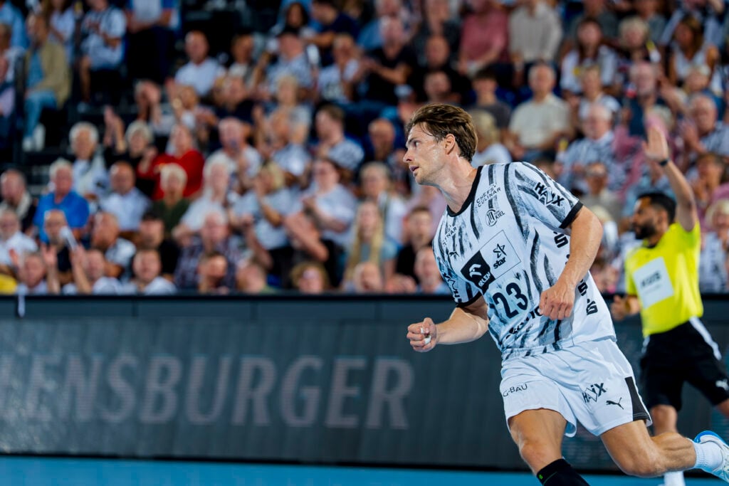 Eric Johansson läuft in einem schwarz-weißen THW-Kiel-Trikot vor einer verschwommenen Zuschauermenge über das Spielfeld.